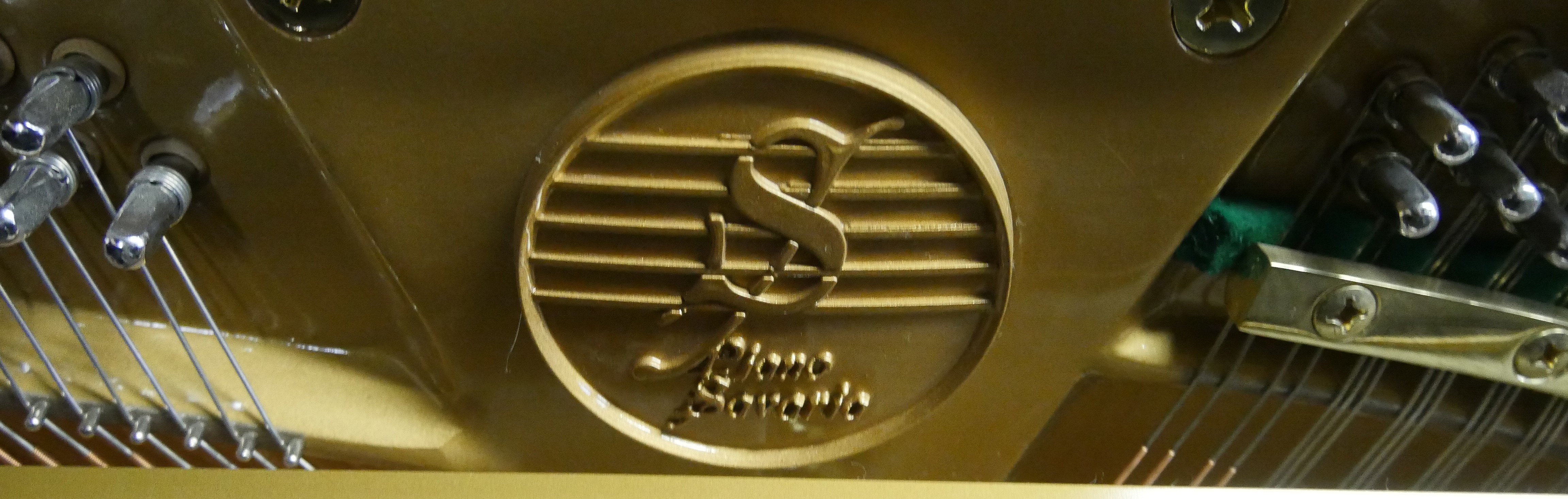 Logo piano Savaria en relief doré à l’intérieur d’un piano, en gros plan